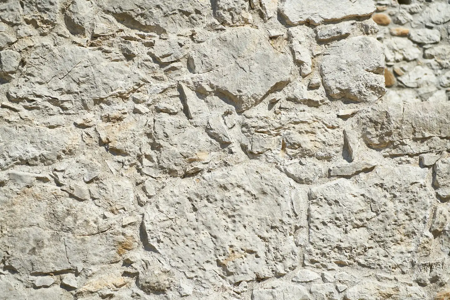 Mur de pierres calcaires claires et irrégulières, enduit de chaux usé entre les pierres