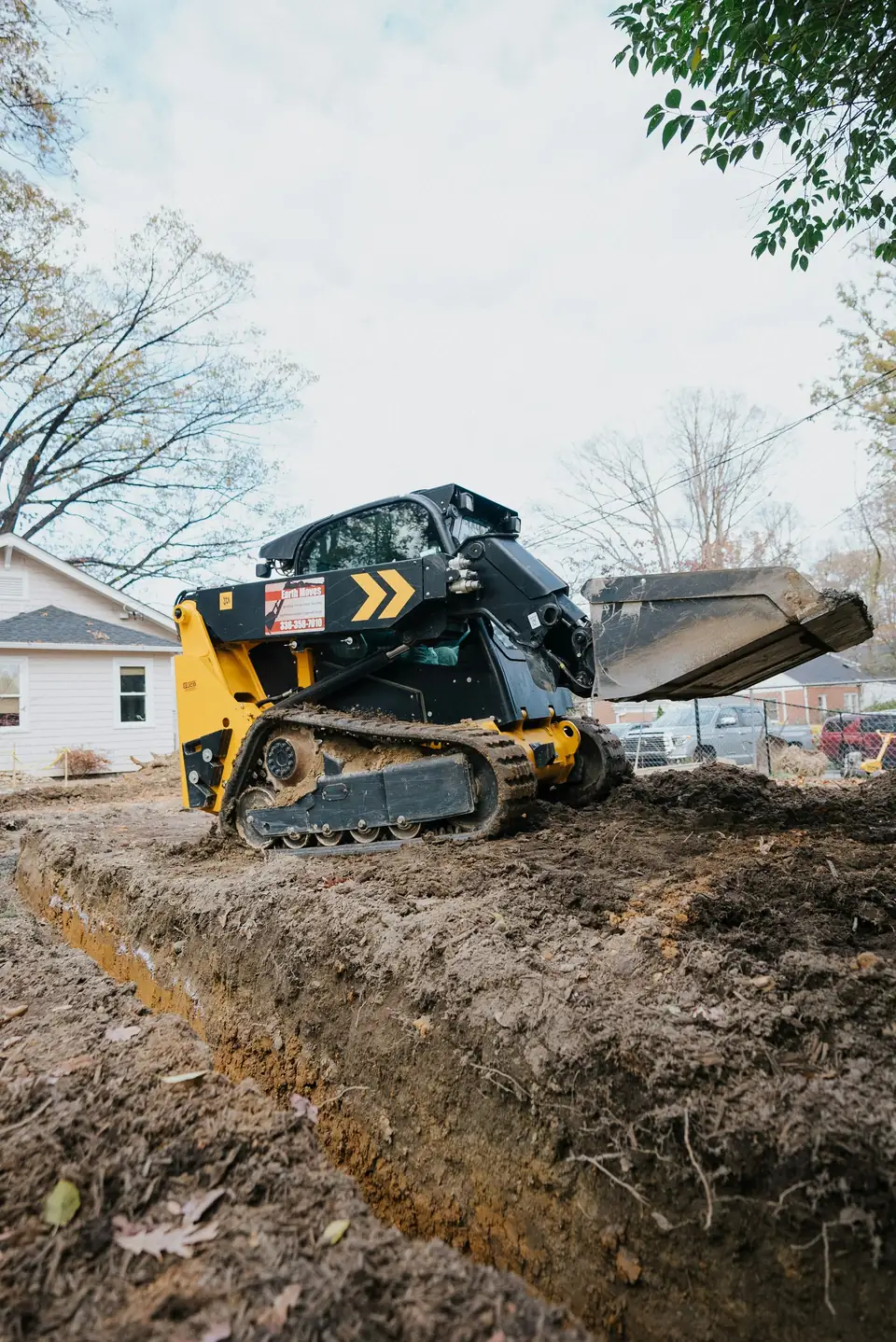 Petite chargeuse sur chenilles qui creuse une tranchée le long d’une maison