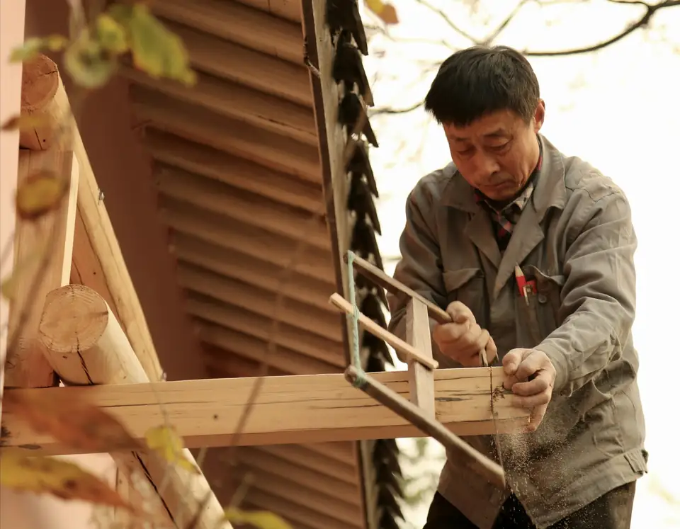 Artisan en veste grise qui ajuste une pièce de bois dans un assemblage