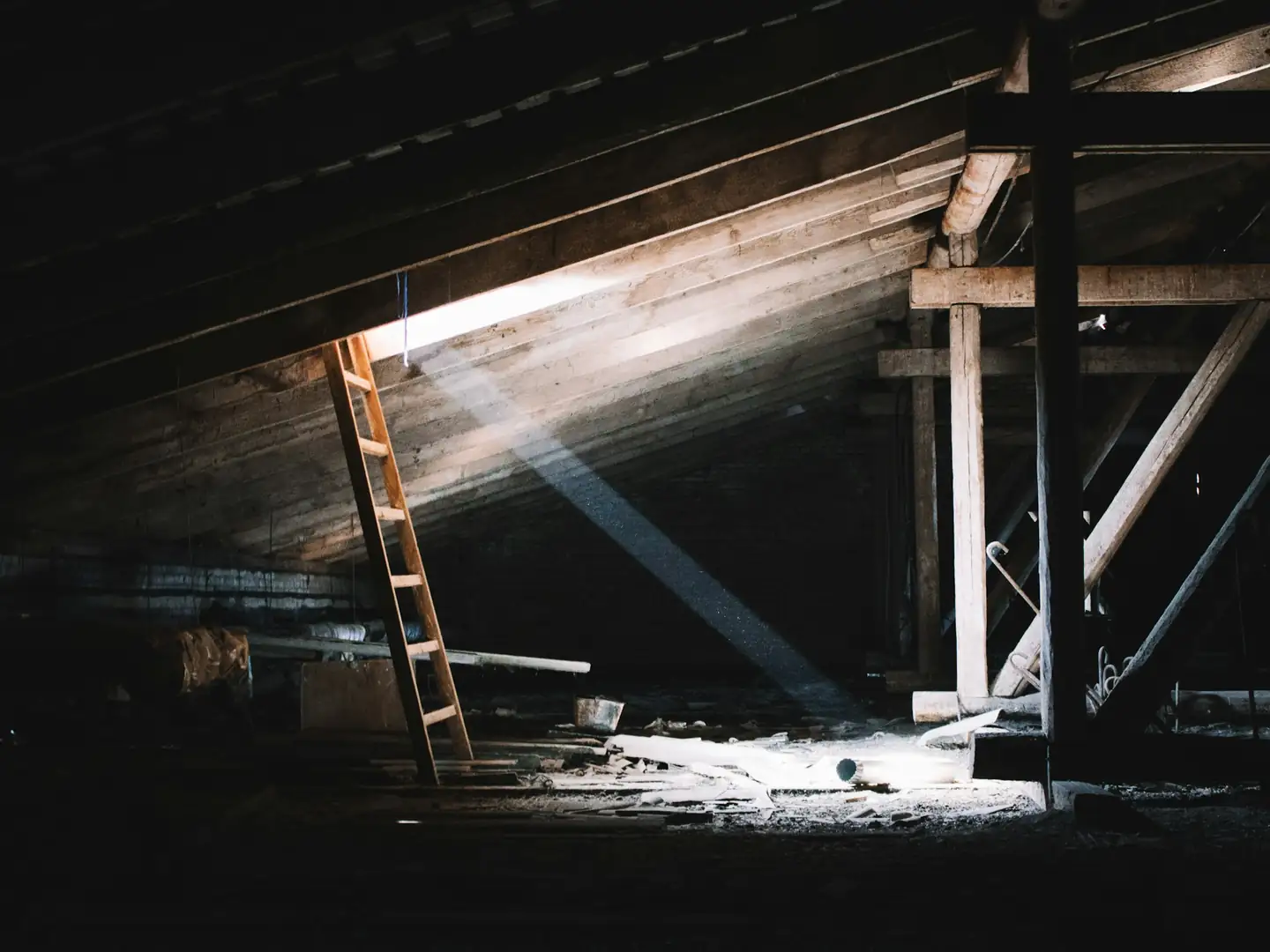 Échelle de bois dans des combles sombres, sous les chevrons, éclairés par un rai de lumière