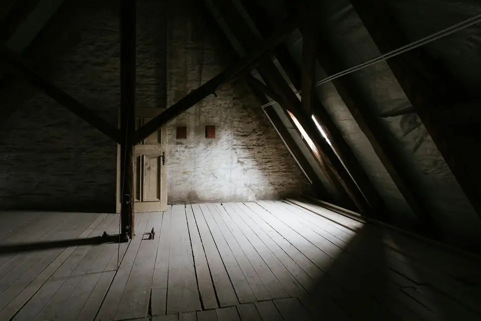 Grenier vide sous une charpente ancienne, plancher de bois et mur de pierre au fond