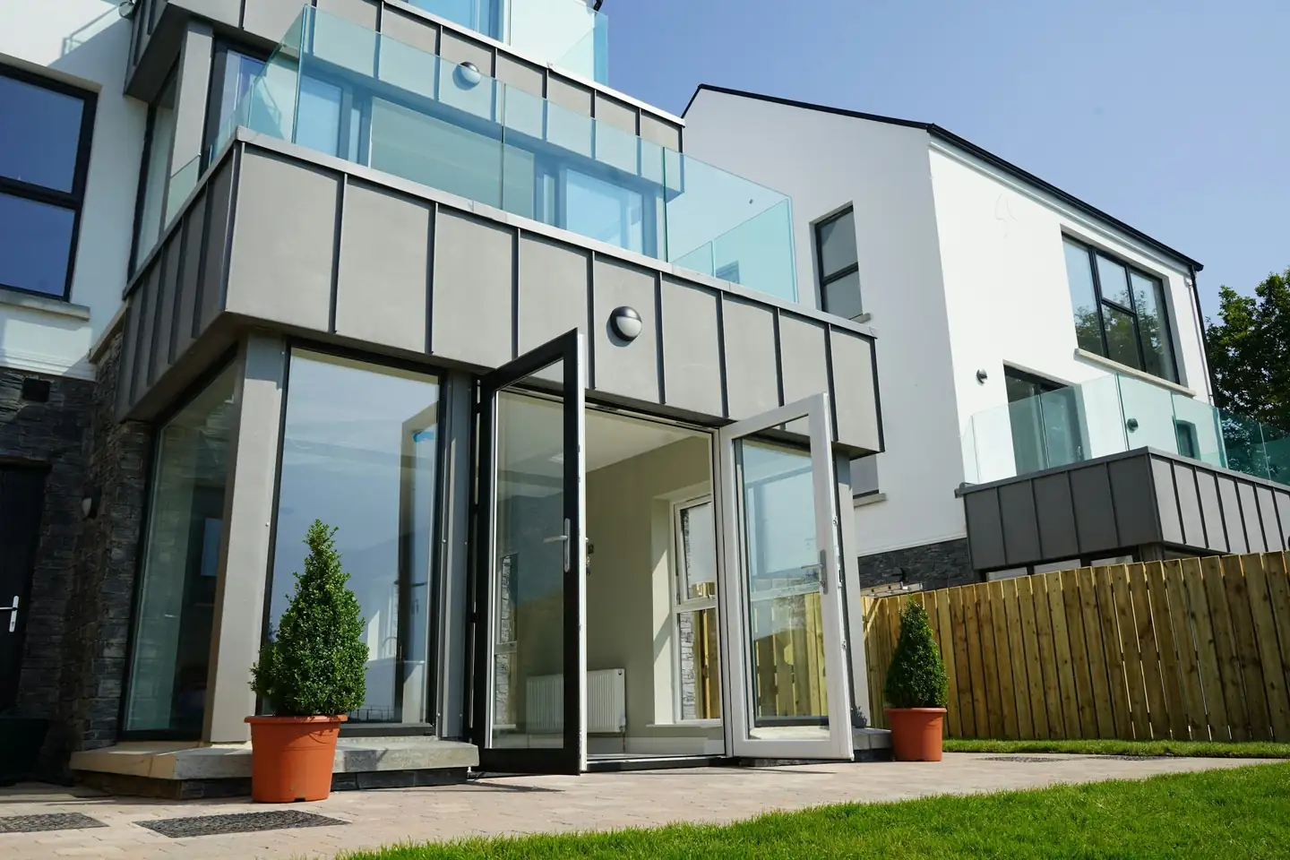 Extension en zinc gris accolée à une maison enduite, portes-fenêtres ouvertes sur le jardin