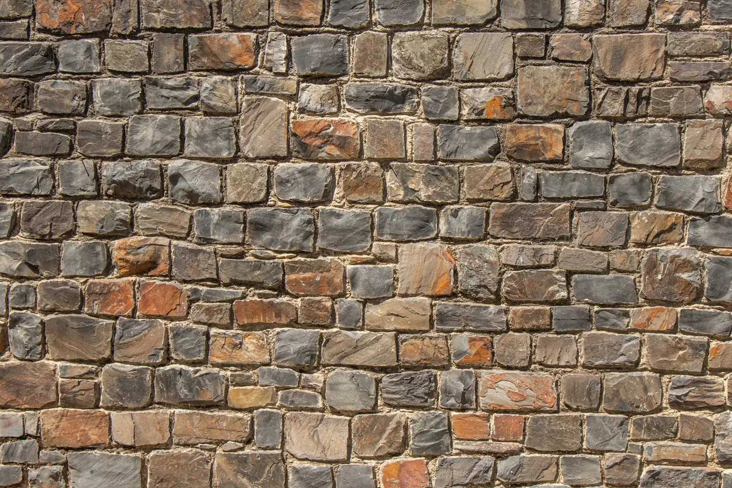 Mur de petits moellons bruns et gris liés par des joints de mortier