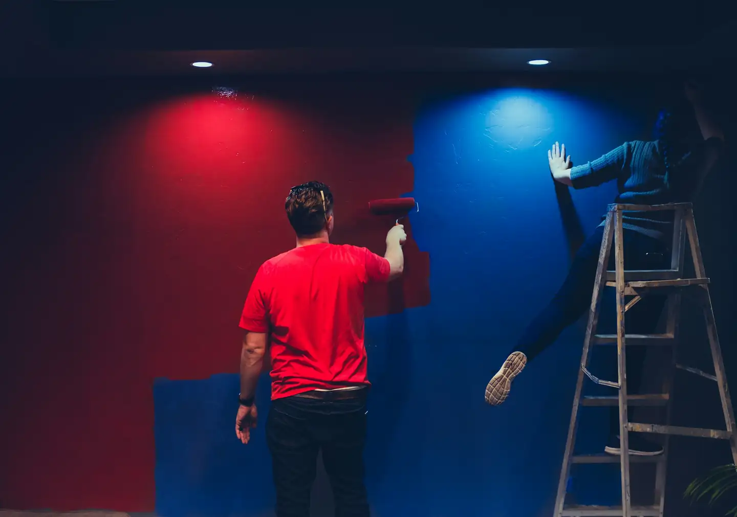 Deux personnes qui peignent l’une un mur rouge, l’autre un mur bleu, depuis un escabeau