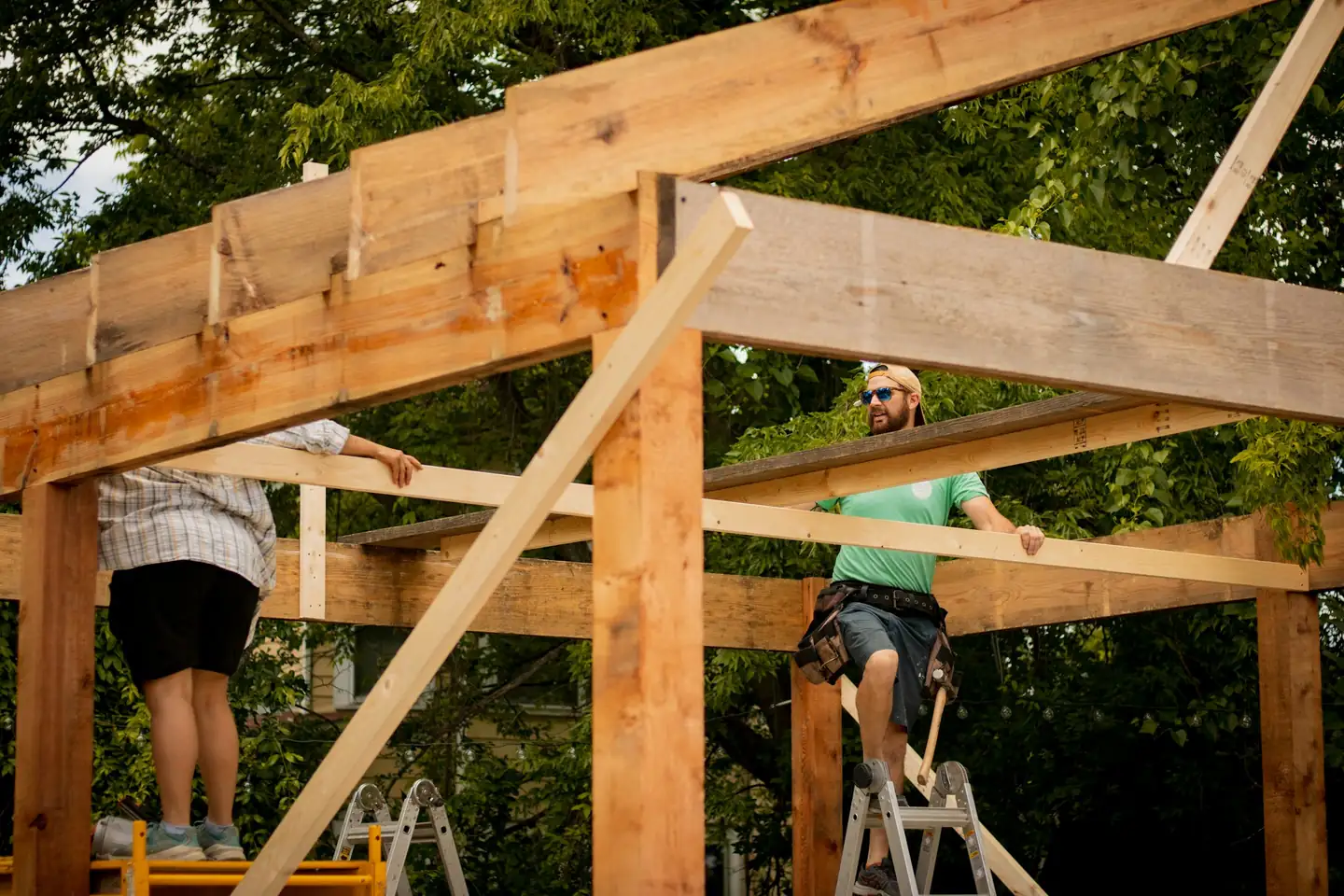 Deux personnes sur des escabeaux qui assemblent une structure de poteaux et de poutres en bois