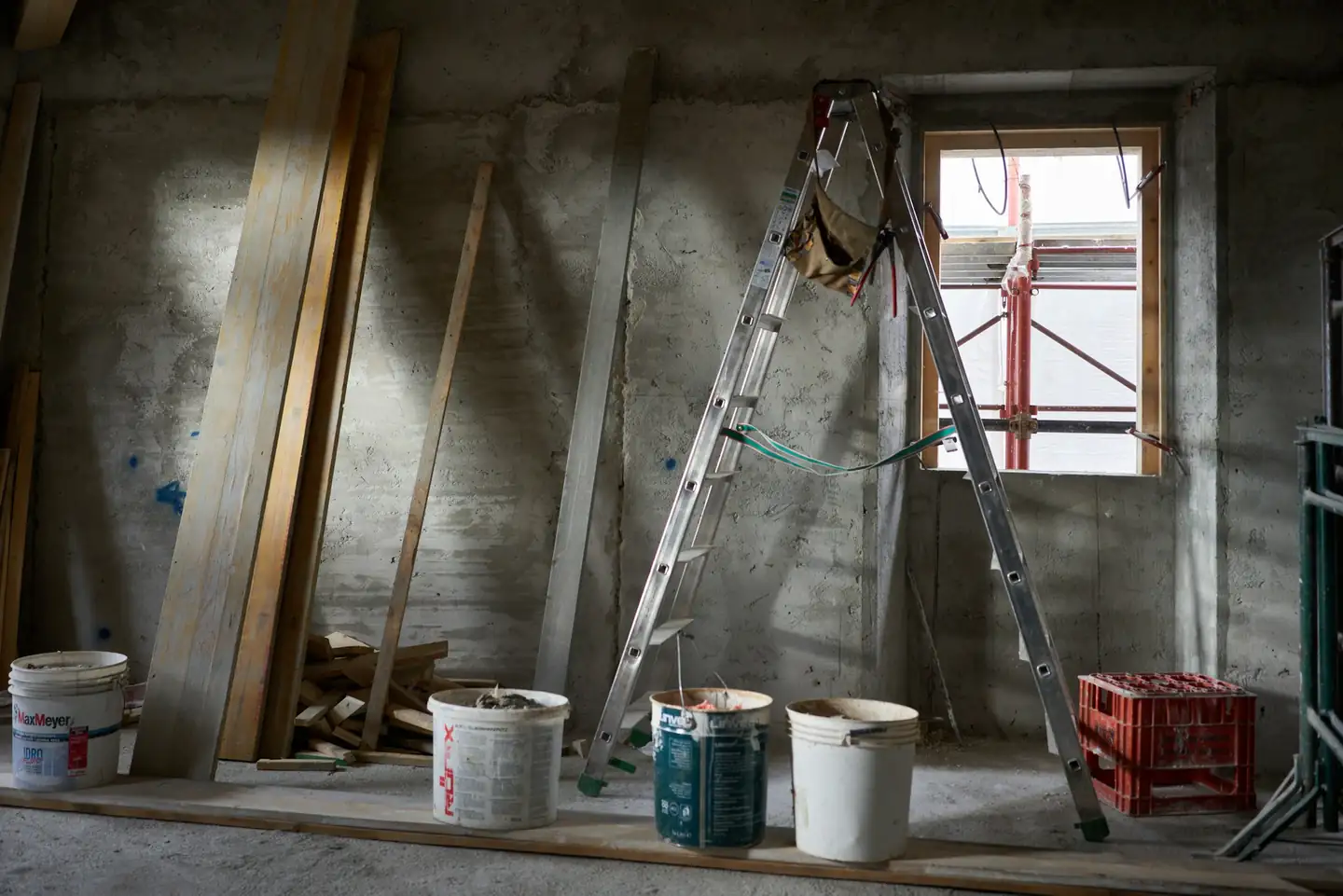 Pièce en travaux avec un escabeau, des seaux de peinture et des murs encore bruts