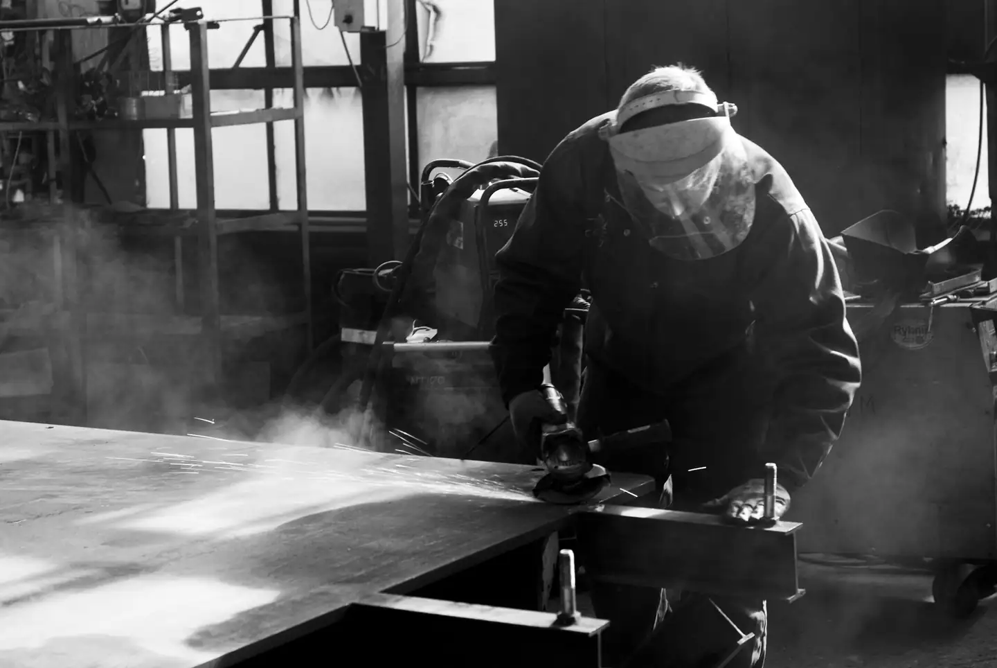 Artisan masqué dans un nuage de poussière au-dessus d’un établi, en noir et blanc