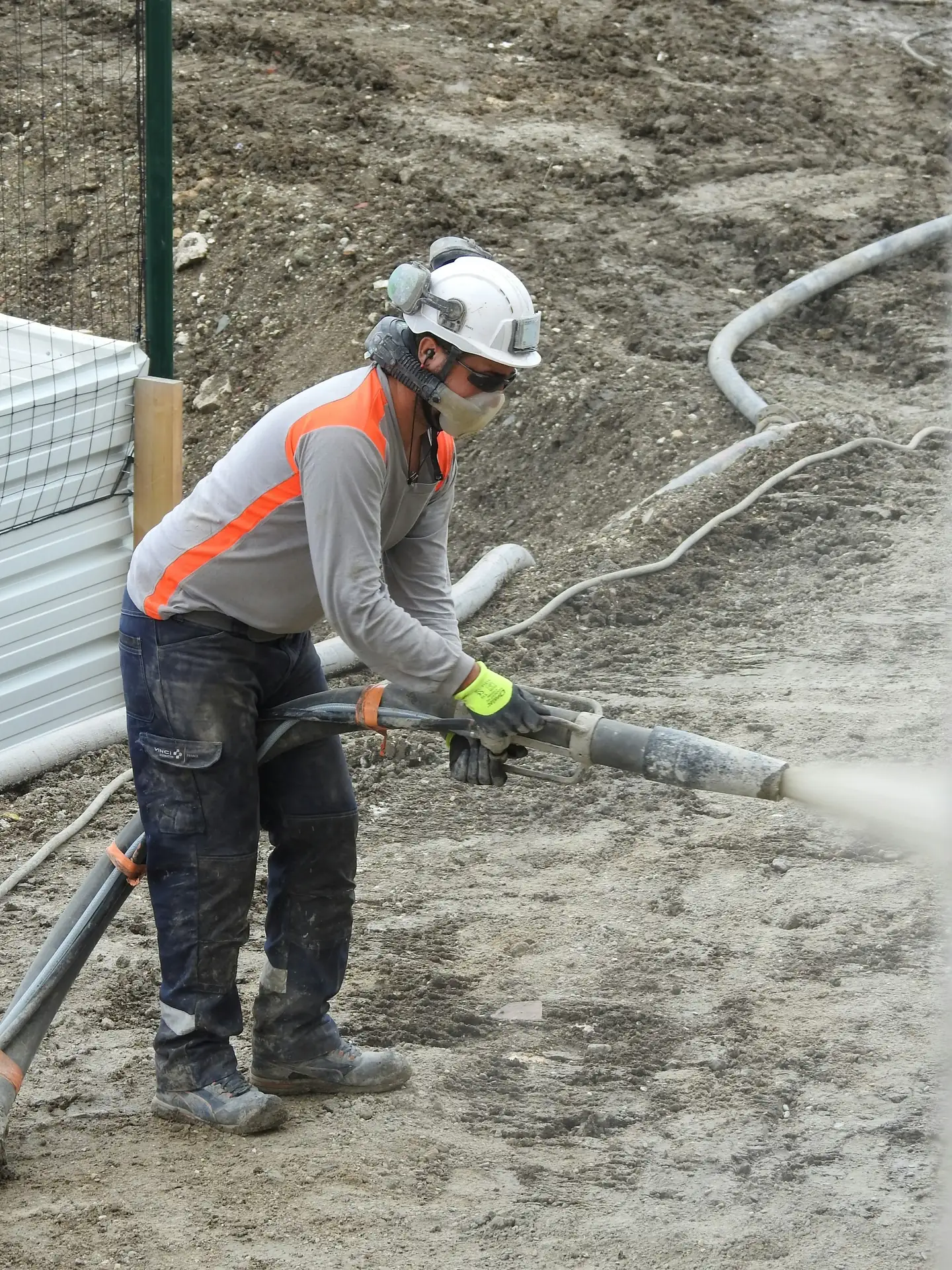 Opérateur casqué et équipé qui dirige une lance de projection sur un chantier