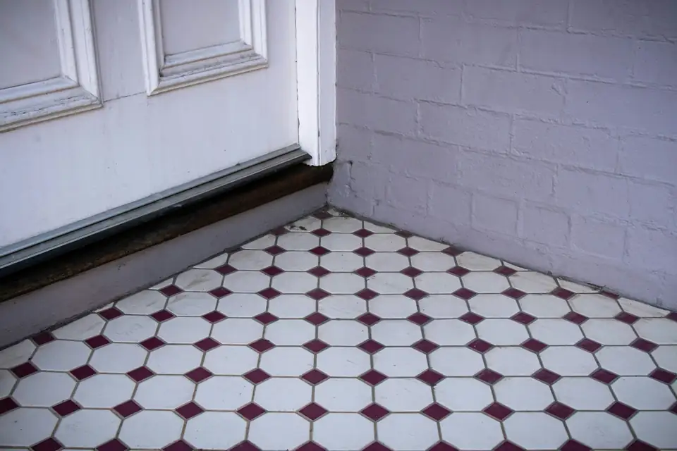 Sol carrelé ancien en octogones blancs et cabochons bordeaux au pied d’une porte